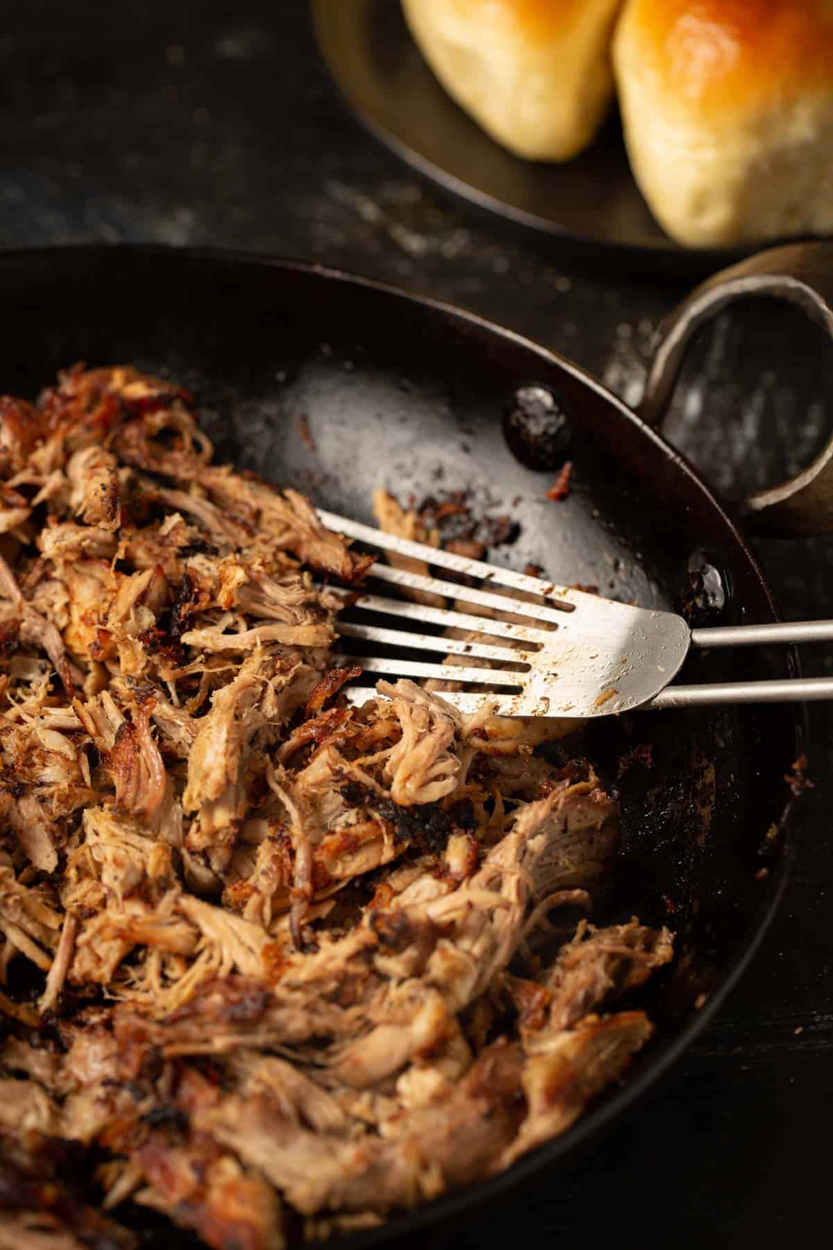 Crispy pork carnitas in a skillet with a spatula.