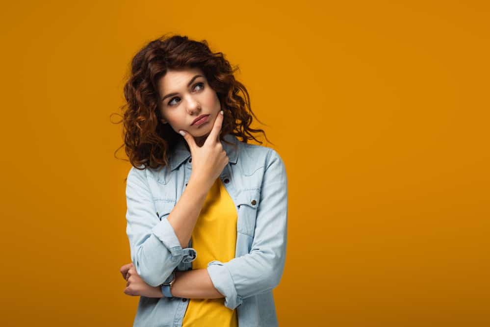 Pensive redhead woman thinking while standing on orange