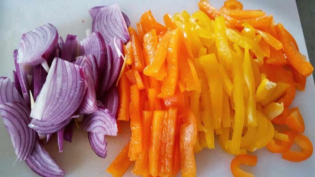sliced red onion and sliced orange bell pepper on a white cutting board