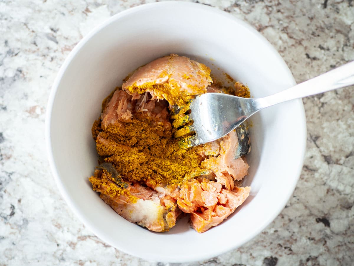 Drained canned salmon in a bowl with a fork and seasonings.