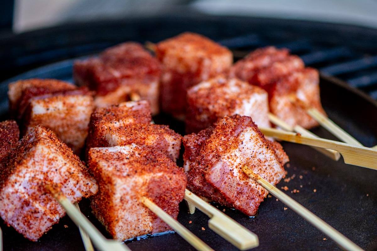 several skewers of bacon chunks on a cast iron skillet on the grill.
