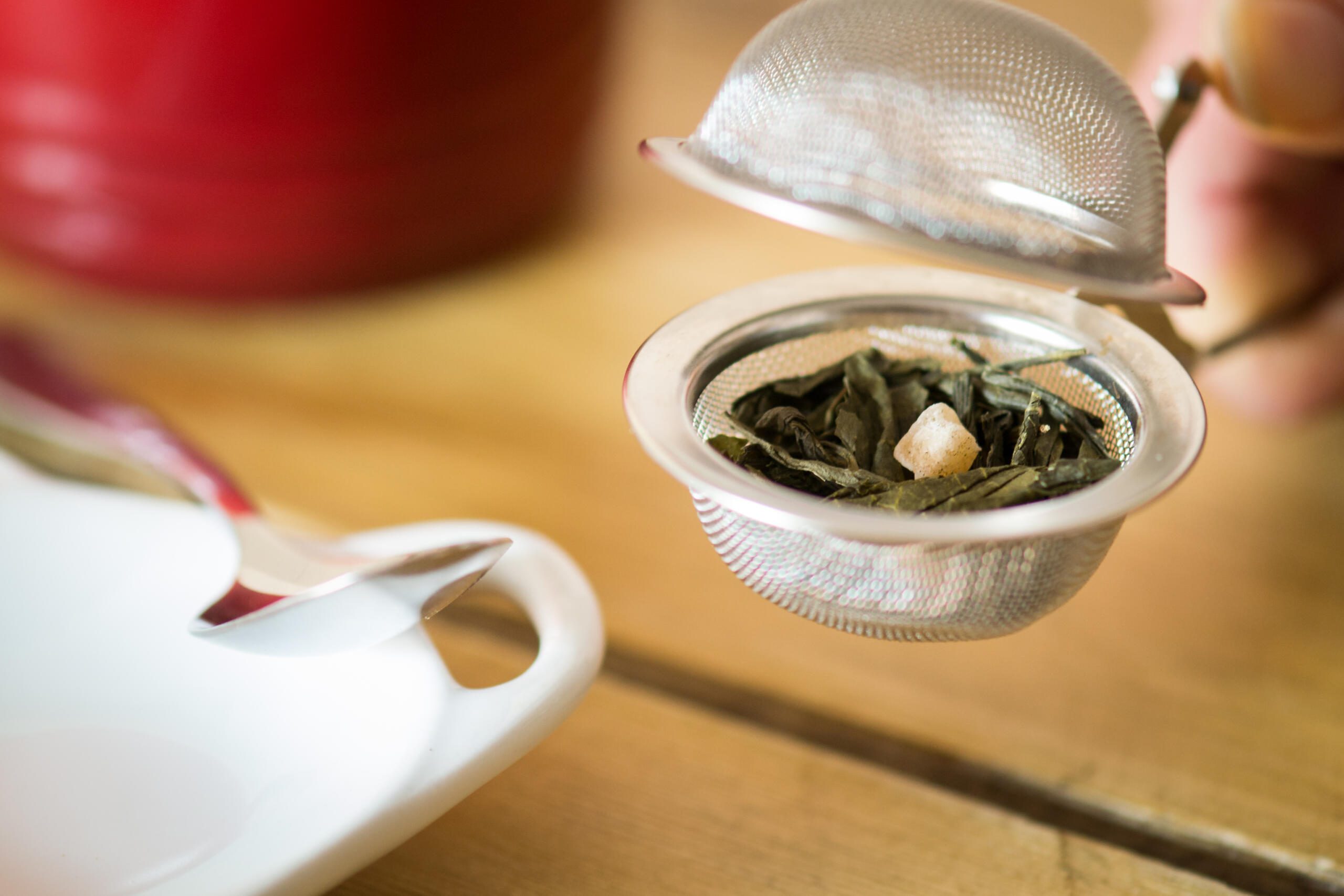 An open loose leaf tea infuser beside tea dish and red mug